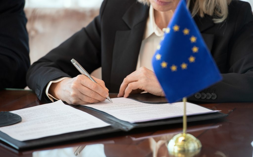 Flag of European Union on table against mature female delegate signing contract